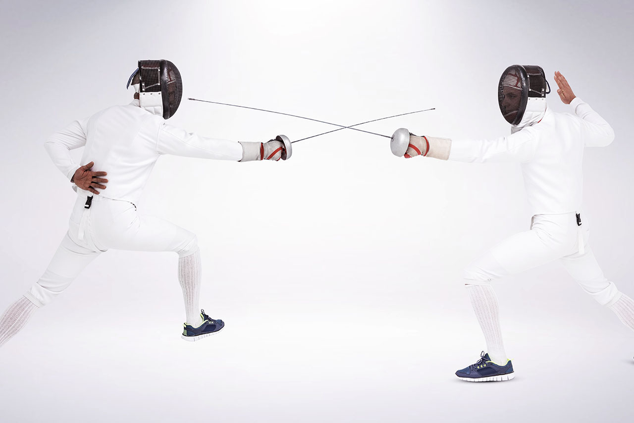 Man wearing fencing suit practicing with sword against grey background