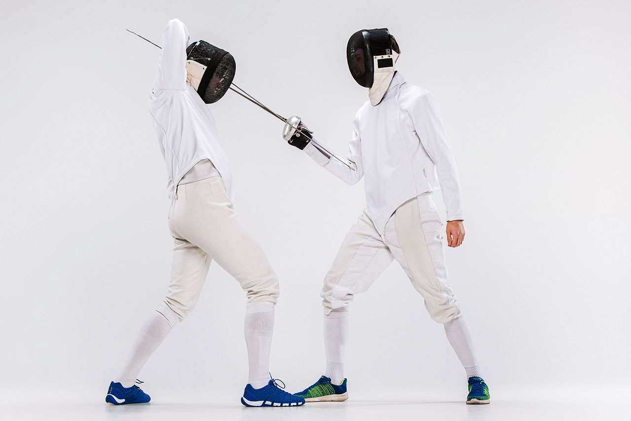 The two men wearing fencing suit practicing with sword against gray
